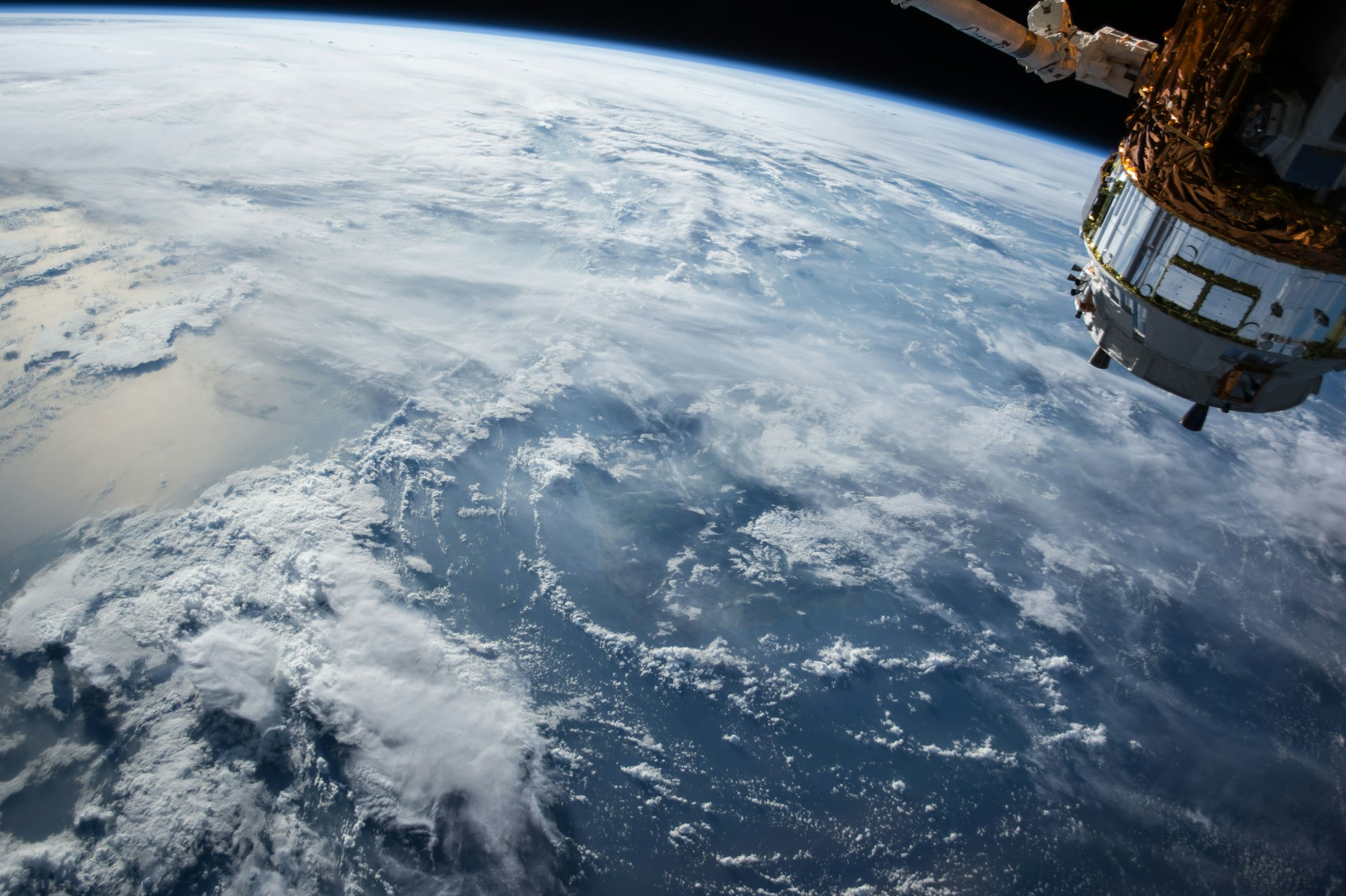 View of Earth from space with a satellite in the upper right corner, showing the planet's curvature, ocean, and scattered clouds.